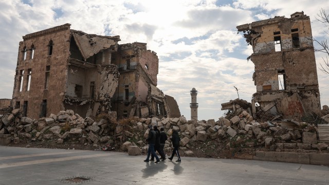 Syrians walk past one of Aleppo's destroyed structures near the northern city's historic citadel.